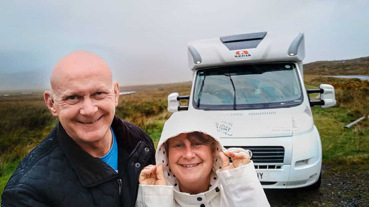 A couple pose smiling in front of a motorhome with moorlands behind them on a motorhome hire holiday.