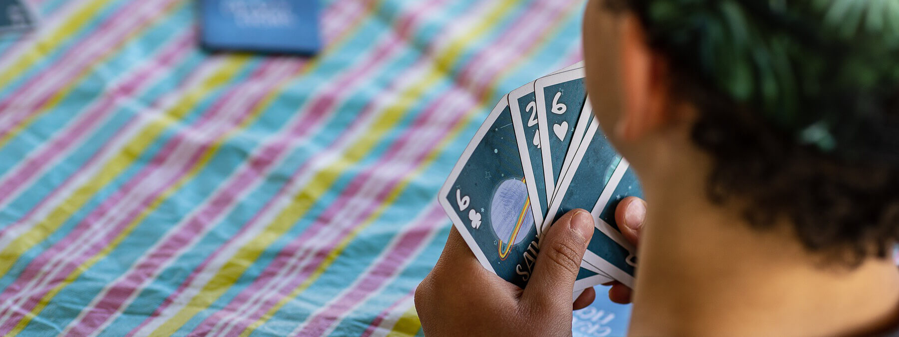 Young boy holding a set of cards in his hand playing a card game on a striped table cloth