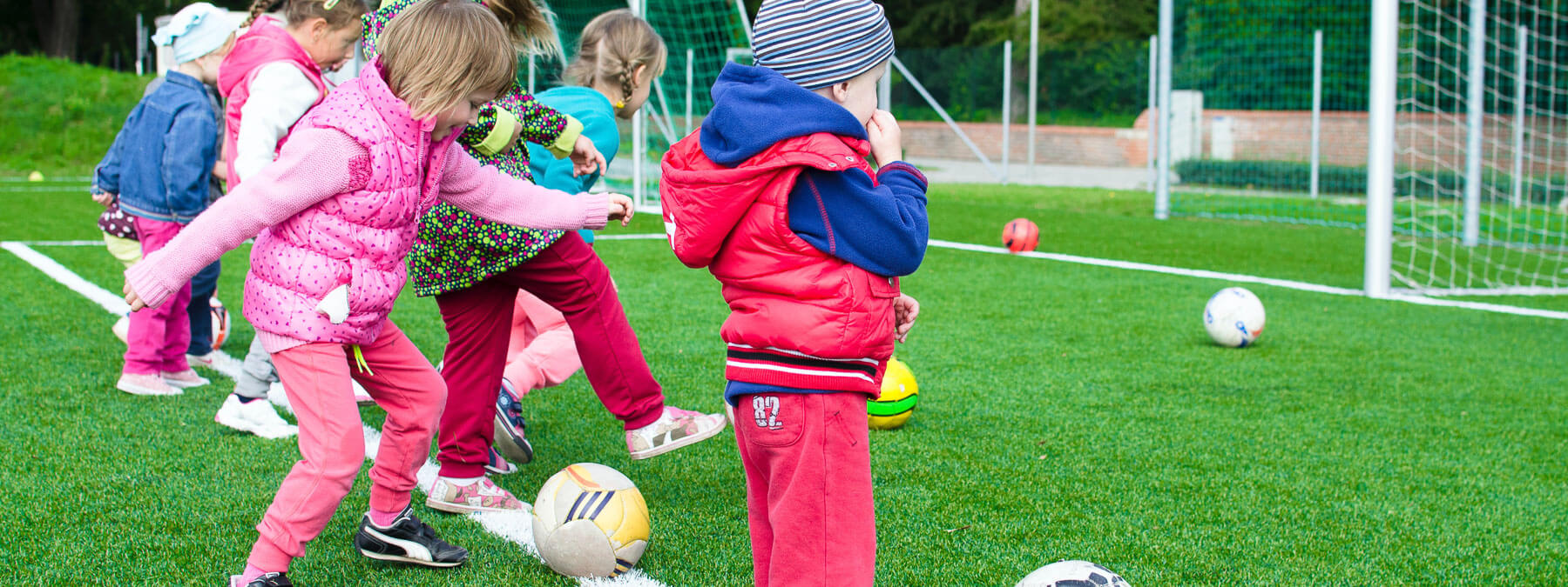 Children stand in a line kicking footballs into a net